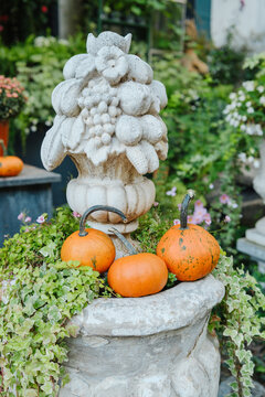 Harvest pumpkins nestled in lush ivy plant decor on stone urn with ornate fruit sculpture