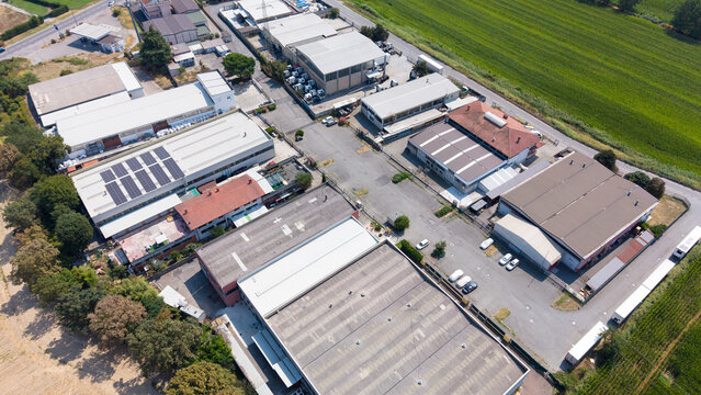 Aerial view of logistics warehouses, production buildings, and workshops in an industrial district with solar panels on rooftops in San Giuliano Milanese, Lombardy, Italy.