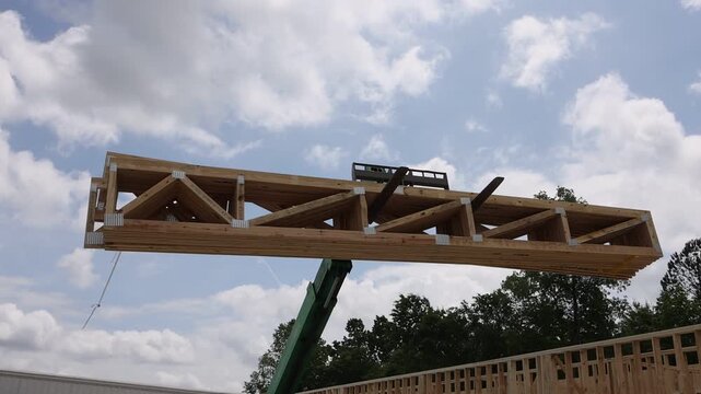 Workers use telehandler lift to position large wooden beams on construction site