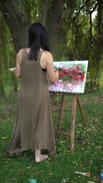 Woman from behind painting outdoors on a canvas and easel, and artist palette