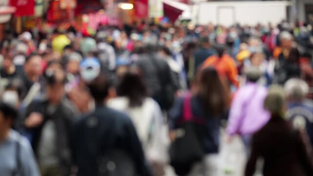 Blurred view, anonymous crowd of people walks along busy pedestrian street of Kai Man Path in Tuen Mun. This daytime, out-of-focus shot captures local shoppers, some wearing face masks