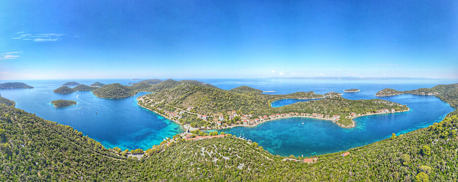 Aerial view of the Lastovo archipelago featuring lush green hills, turquoise waters, and a charming coastal village with red-roofed houses in Lastovo, Dubrovnik-Neretva County, Croatia.