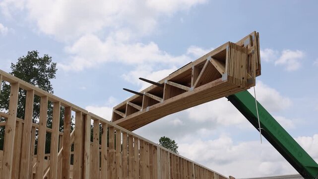 Workers use crane to lift wooden structures for building under construction in wooded area