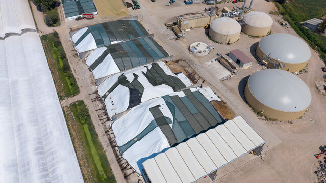 Aerial view of silage bunkers covered with white and green plastic sheets at an agricultural farm, with large biogas digester tanks in Peschiera Borromeo, Lombardy, Italy.