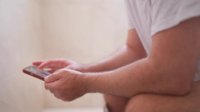 Man sitting on the toilet using a smartphone for scrolling social media, checking messages, playing games, and browsing the internet, illustrating addiction and procrastination