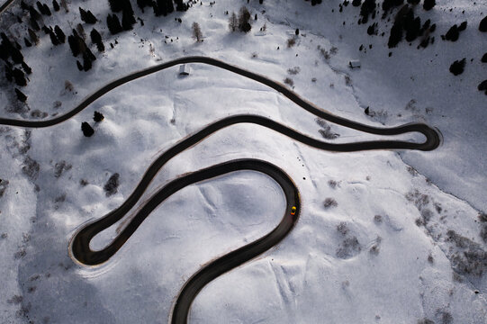 Aerial view of Gardena Pass with a winding road cutting through snow-covered mountain slopes in Corvara, Trentino-Alto Adige, Italy.