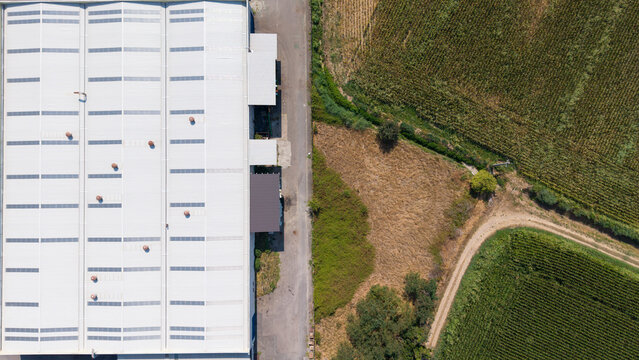 Aerial view of a cold finished steel manufacturing facility with a large metal roof and adjacent agricultural fields in Milan, Lombardy, Italy.