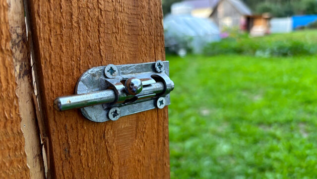 Close-up of metal barrel bolt latch installed on wooden door with green garden background
