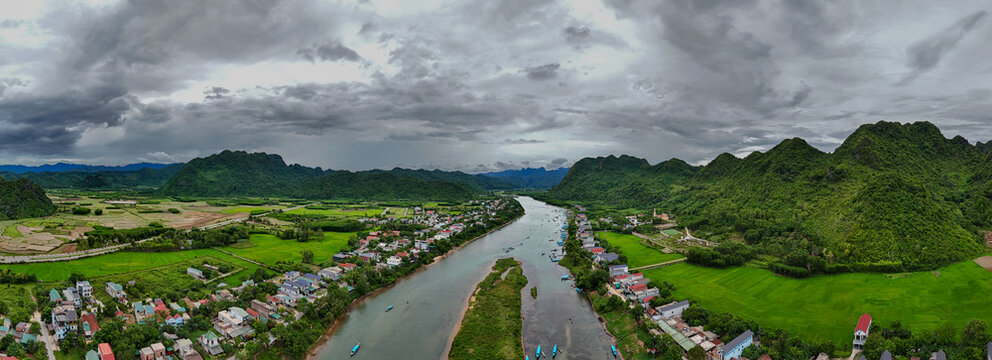 Aerial view of Phong Nha - near Ke Bang National Park with a river winding through a lush green valley, small village, and rice fields in Phong Natural Heritage Area, Quang Tri, Vietnam.