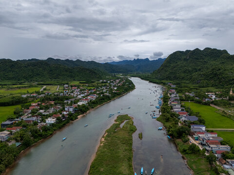 Aerial view of Phong Nha - near Ke Bang National Park with a winding river, lush mountains, small boats, and village houses under a cloudy sky in Phong Natural Heritage Area, Quang Tri, Vietnam.