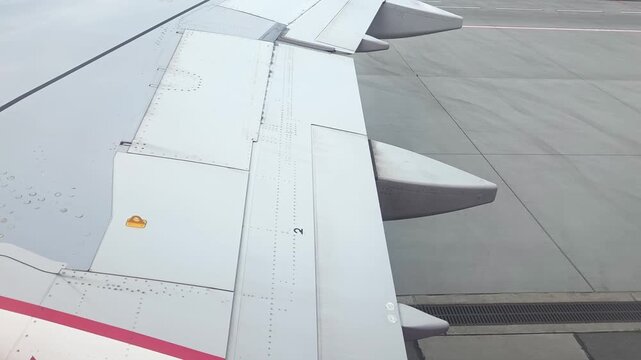 Aircraft wing with flaps extended and engines visible during taxiing on runway, showcasing details of wing structure and markings in an airport setting