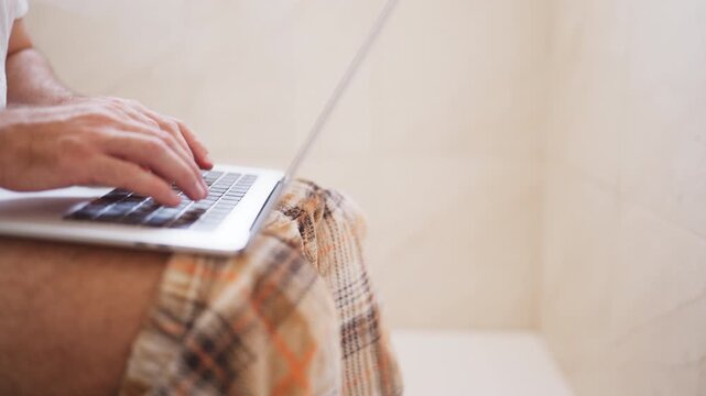 Businessman working remotely on laptop while sitting in bathroom, showing the flexibility of modern remote work, digital employment and ability to work from unconventional locations.