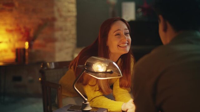 Cheerful red-haired woman laughs while talking with boyfriend in coffee shop