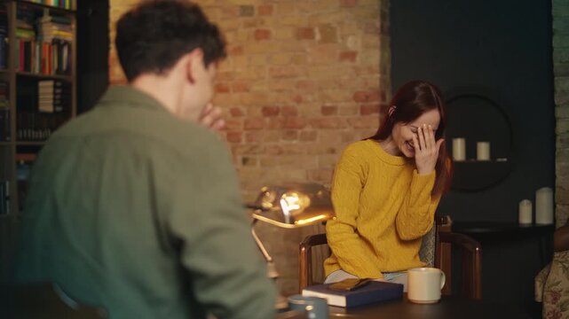 Joyful red-haired woman and boyfriend laugh while talking in cozy coffee shop