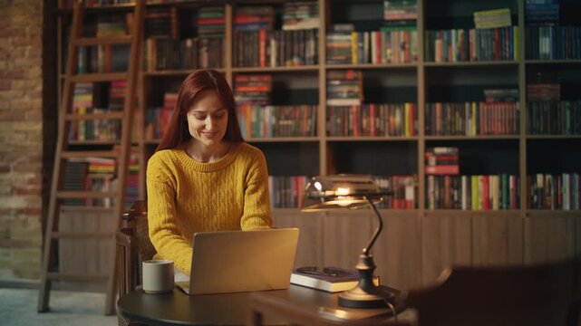 Inspired young female author types on laptop in library, working on new book