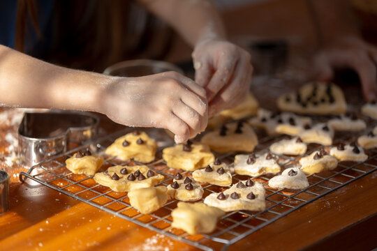 Child hand careful decorate shape cookie with chocolate chip on cooling rack in warm bright kitchen showing joyful focus during fun home bake activity on wooden table