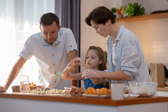 Happy family mother father child daughter baking cooking together in kitchen with joyful expression bonding lifestyle at home enjoying culinary activity making food