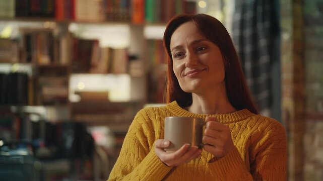 Smiling red-haired woman drinks tea while relaxing in cozy bookshop cafe