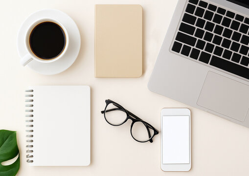 Stylish flat lay with laptop, coffee cup, smartphone, notebooks, pen, glasses, and green leaf on light background. Perfect workspace concept for business, blogging, and creative projects.
