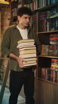 Happy young man holds stack of books and smiles, enjoying his reading hobby