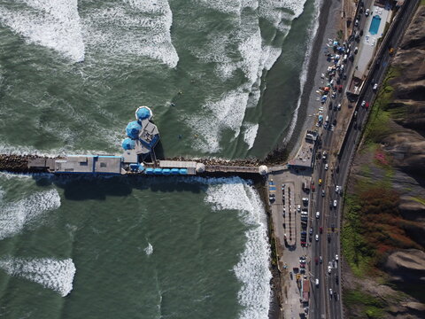 Aerial view of Restaurante La Rosa Nautica extending into the Pacific Ocean with crashing waves and a busy highway along the shoreline, Miraflores, Provincia de Lima, Peru.