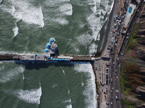 Aerial view of Restaurante La Rosa Nautica extending into the Pacific Ocean with crashing waves, coastal cliffs, and a nearby highway in Miraflores, Provincia de Lima, Peru.