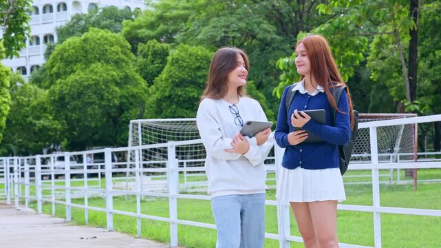 Student woman campus tablet book walkway fence green education friendship outdoor digital learning, young women smiling near trees with notebook and relaxed conversation
