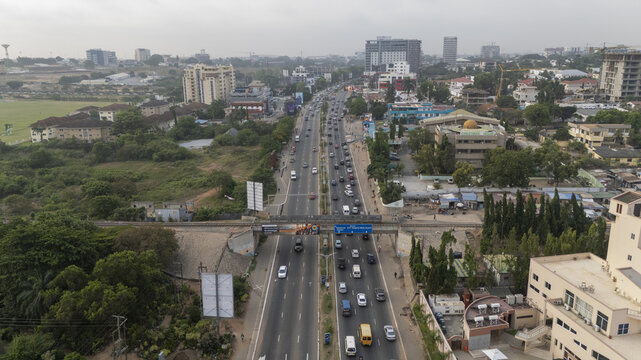 Aerial view of a busy multi-lane highway with traffic, a railway bridge, commercial buildings, and greenery in Accra, Greater Accra Region, Ghana.
