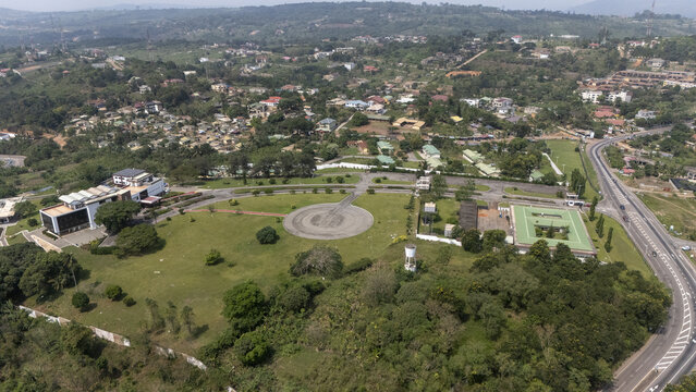 Aerial view of the Aburi area featuring a large green lawn, a circular paved plaza, modern buildings, and surrounding lush vegetation with a winding road in Aburi, Eastern Region, Ghana.