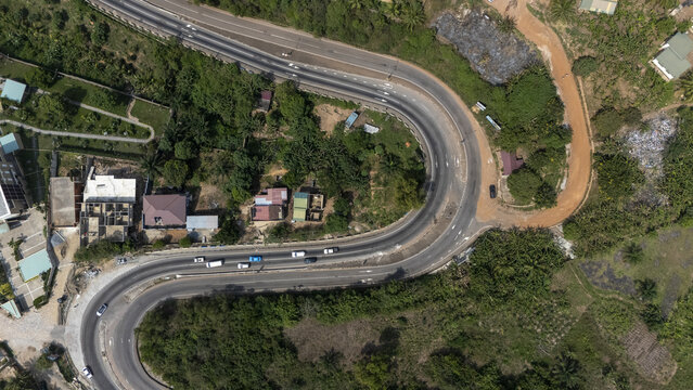 Aerial view of a winding asphalt road cutting through lush green vegetation and scattered buildings in the hilly landscape of Aburi, Eastern Region, Ghana.