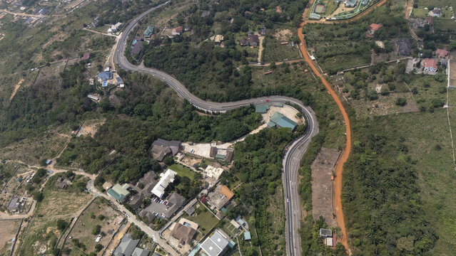 Aerial view of the winding road through the lush green hills and residential areas of Aburi, Eastern Region, Ghana.