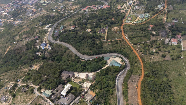 Aerial view of a winding road cutting through the lush green hills with scattered residential buildings and dense vegetation, Aburi, Eastern Region, Ghana.
