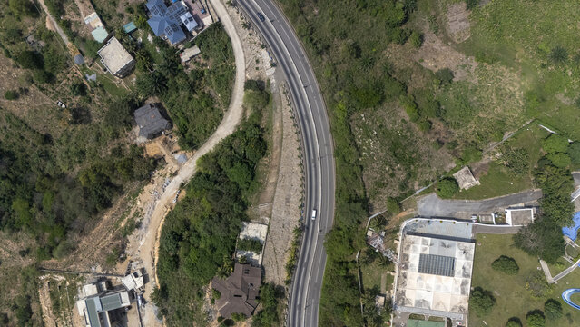 Aerial view of a winding road cutting through the lush green landscape with scattered buildings and dense vegetation in Aburi, Eastern Region, Ghana.