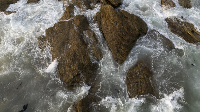 Aerial view of Sakumono Beach with rugged rocks surrounded by crashing ocean waves and white sea foam in Sakumono, Greater Accra Region, Ghana.