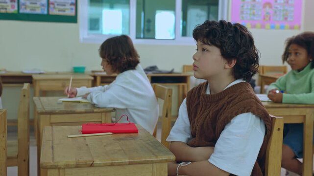 Curly hair child classroom student desk education school learning sitting writing with notebook pencil at wooden desk in bright primary classroom lesson with attentive pupil and classmates