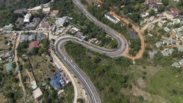 Aerial view of the winding mountain road in Aburi, surrounded by lush vegetation, scattered residential houses, and rolling hills in Aburi, Eastern Region, Ghana.