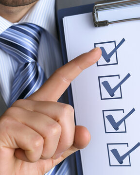 Checklist in Hand: A close-up shot captures a businessman's hand pointing to a completed checklist, symbolizing organization and efficiency in a professional setting.