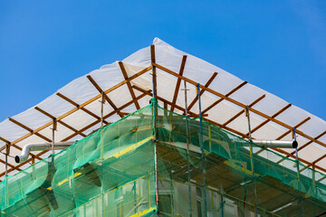 Old building roof covered with scaffolding netting during renovation © Mariia