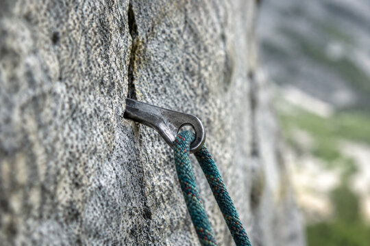 A steel climbing piton in granite with a rope, natural daylight.