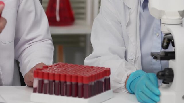 Scientists Hands Holding Blood Sample Vials and Adjusting Microscope in Laboratory