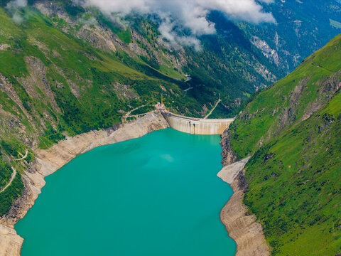 Aerial view of Stausee Mooserboden reservoir with its concrete dam nestled between steep green mountain slopes in Kaprun, Salzburg, Austria.