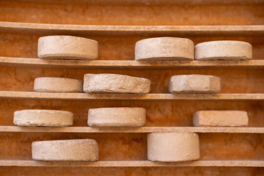 Multiple round and octagonal clay prayer stones, known as Turbah or Mohr, neatly arranged on wooden shelves inside a traditional Iranian mosque or shrine.