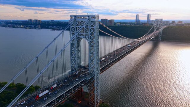Afternoon sunlight on George Washington Bridge, New York. Drone perspective of steel suspension structure across Hudson River with traffic and glinting water.