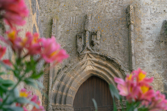 Portail gothique en pierre sculpt&eacute;e avec fleurs roses en premier plan, Bazens