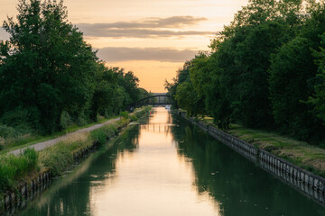 Fototapeta premium Canal paisible bordé d'arbres au coucher du soleil avec pont
