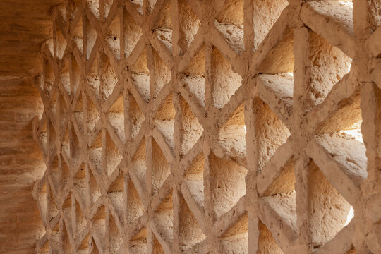 Detailed close-up of an intricate geometric lattice wall (Fakhr-o-Madian) crafted from mud brick and plaster, located within the historic Jameh Mosque of Ardestan in Isfahan Province, Iran.