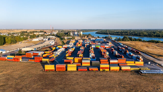 Aerial view of a busy industrial port area with rows of colorful shipping containers, warehouses, and a river flowing through the landscape in Sremska Mitrovica, Vojvodina, Serbia.
