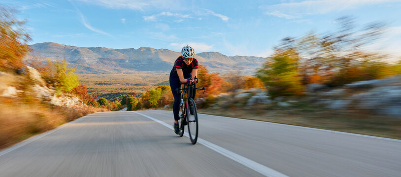 Female Cyclist Riding Road Bike on Mountain Road During Autumn Training Session