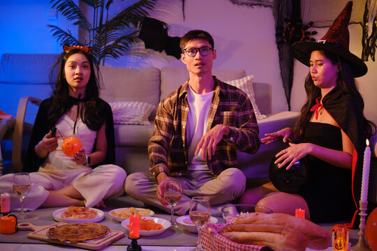 Young Asian friends eating popcorn and snacks during a Halloween party.