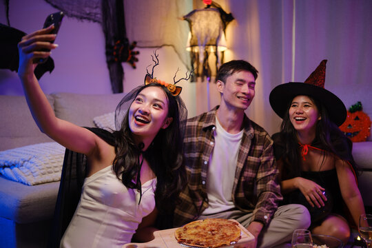 Young Asian friends taking a smartphone selfie with pizza at a Halloween party.